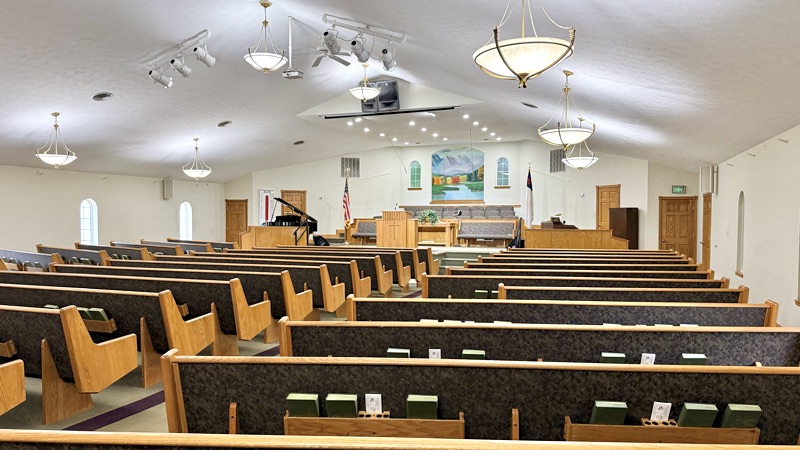 Sanctuary interior, showing rows of wooden pews, pulpit with cross, grand piano, and scenic mural behind the platform