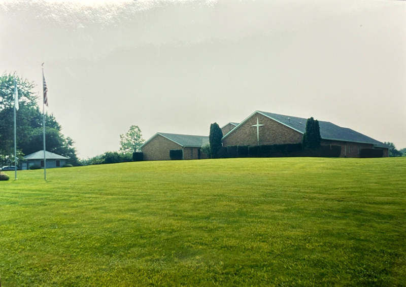 Huber Heights Baptist Temple church exterior, brick building with white cross, American flags, and green lawn, vintage photo
